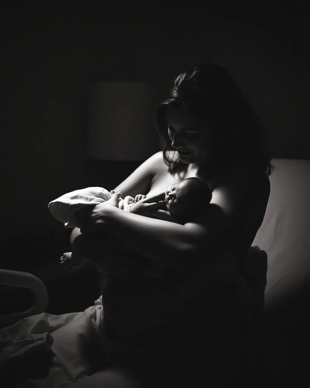 Documentary photograph of a mother holding her newborn moments after birth, in warm sepia tones.